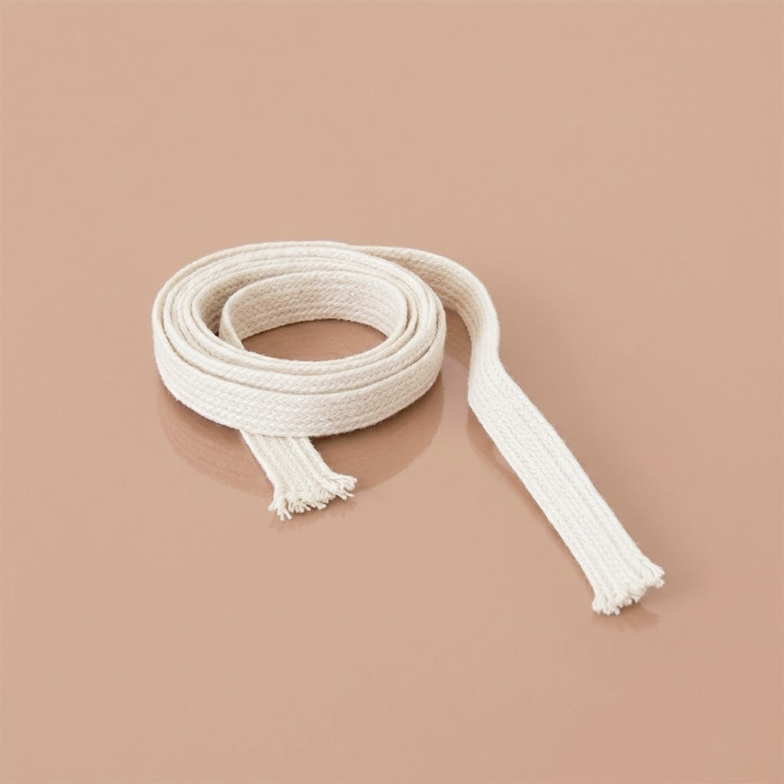 Rouleau de mèche plate en coton pour bougies, déroulé sur fond beige