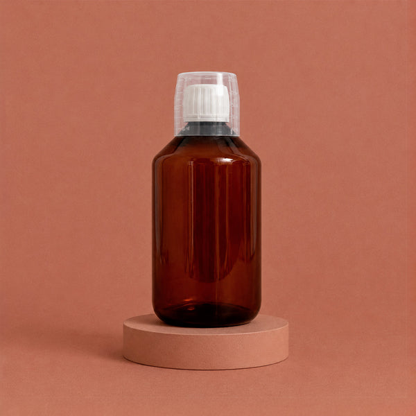 Bouteille ambrée pour lessive avec son bouchon doseur sur socle rose