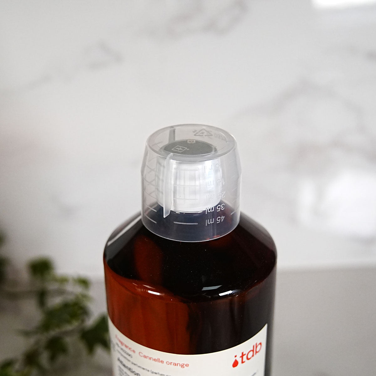 Gobelet doseur gradué devant un flacon de parfum ambré