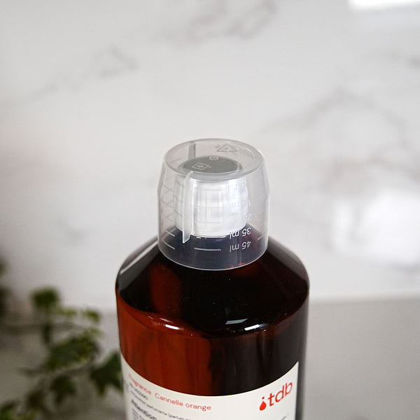 Gobelet doseur gradué devant un flacon de parfum ambré