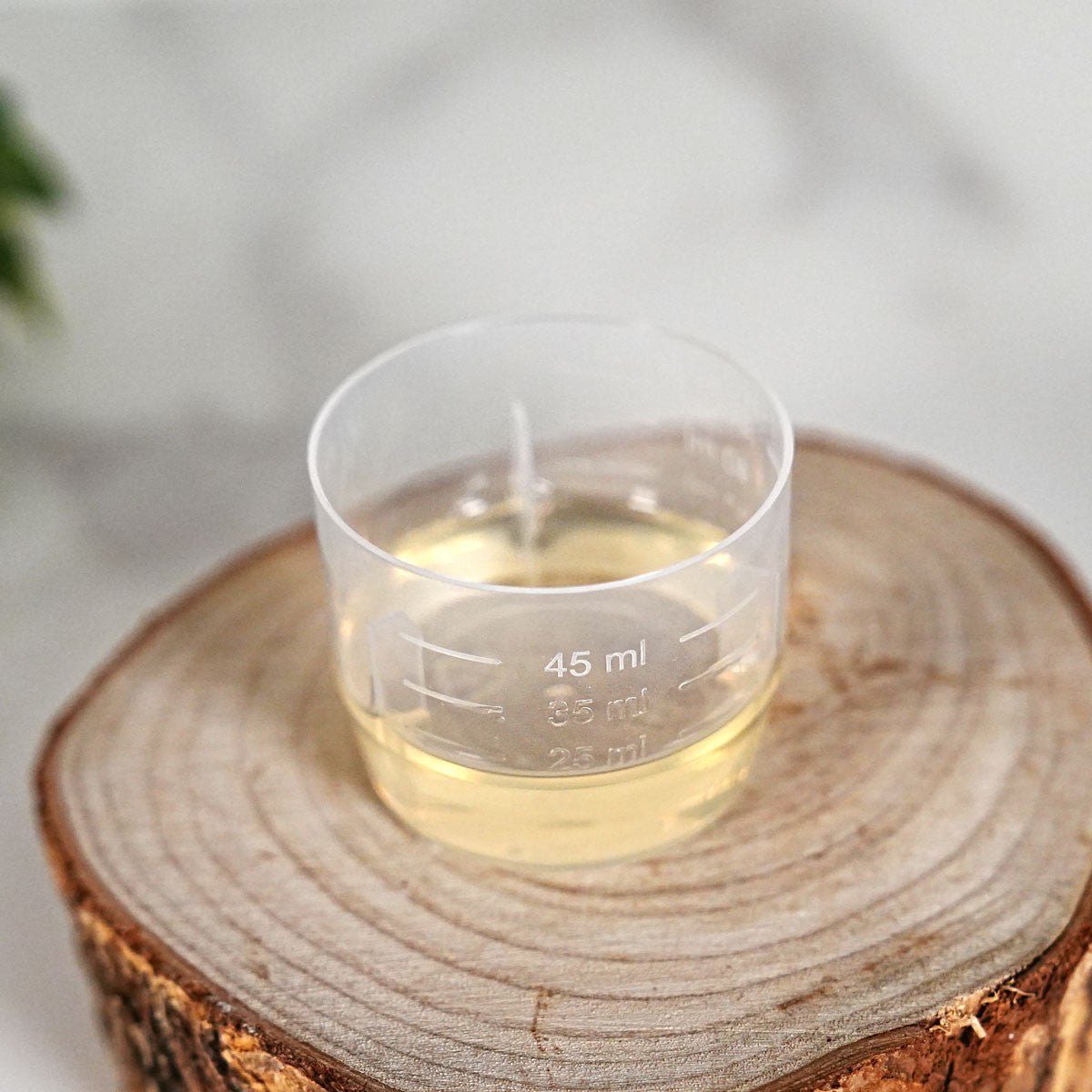 Gobelet doseur gradué de 0 à 50 ml rempli de parfum, sur rondin de bois
