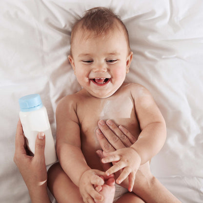 Bébé souriant tenant un flacon de talc, ambiance du parfum Talco
