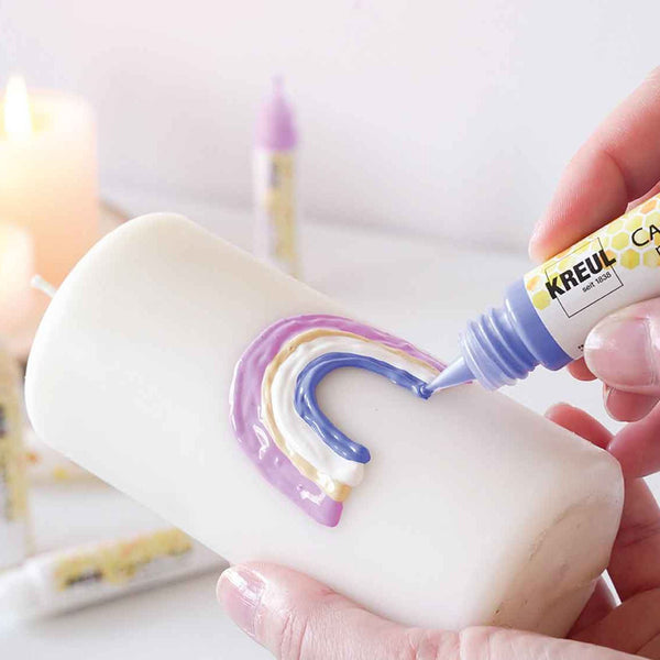 Main dessinant un arc-en-ciel sur une bougie avec un stylo Stylos à Bougie