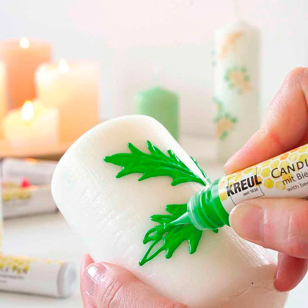 Main dessinant un feuillage vert sur une bougie avec un stylo Stylos à Bougie